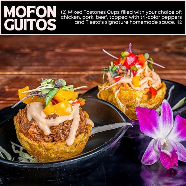 Two Mofonguitos, one with chicken and one with beef, topped with sauce and peppers, next to an orchid.