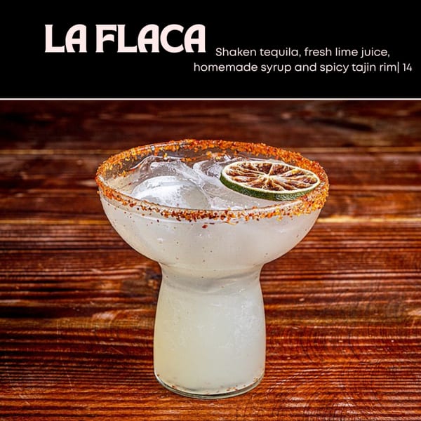 A La Flaca cocktail, a margarita with a tajin rim and lime slice, on a wooden table.