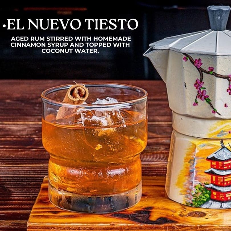 El Nuevo Tiesto cocktail, an aged rum drink with cinnamon and coconut water, next to a decorative coffee pot.
