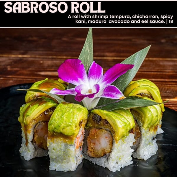 Sabroso Roll with shrimp tempura, chicharron, spicy kani, maduro avocado, and eel sauce, garnished with an orchid.