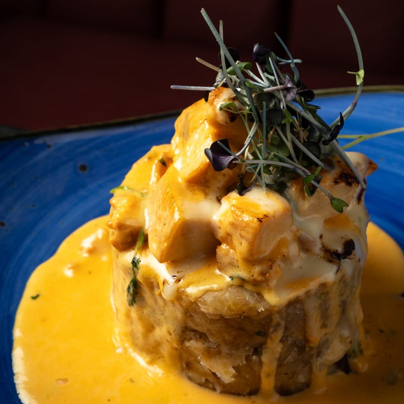 Savory chicken and mashed plantain dish, topped with microgreens and a rich orange sauce on a blue plate.