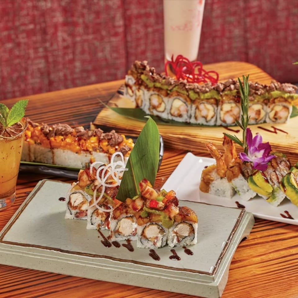 Assortment of El Tiesto Cafe's Latin-American sushi rolls with various toppings and sauces on wooden tables.