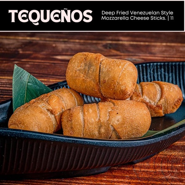 Golden-brown tequeños, deep-fried Venezuelan mozzarella cheese sticks, served on a black platter with a green leaf.