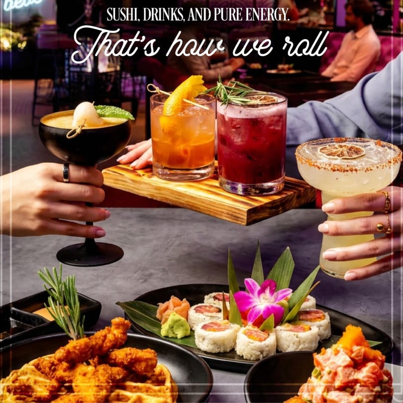 Hands holding cocktails and a wooden tray of drinks, with sushi and chicken and waffles on a table.