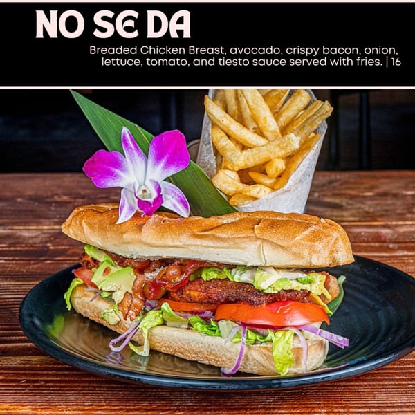 A "No Se Da" sandwich with breaded chicken, avocado, bacon, and vegetables, served with fries.