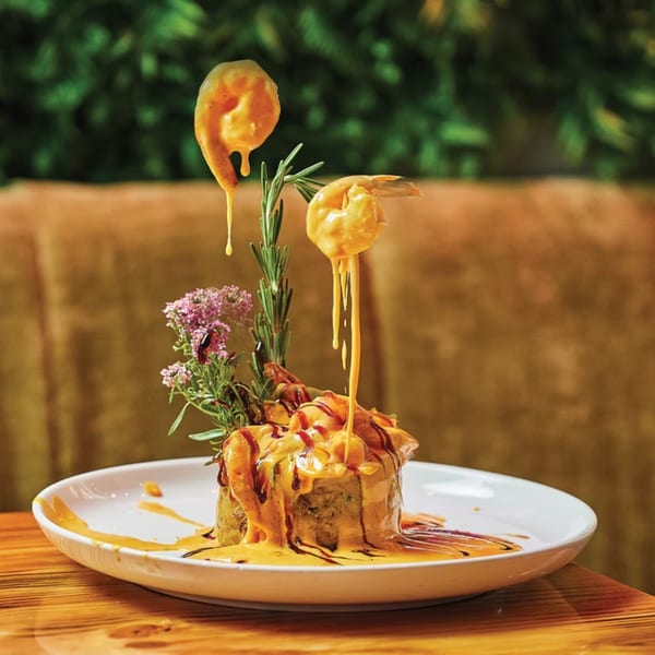 Latin-American mofongo dish with shrimp and sauce drizzling, garnished with rosemary and flowers.