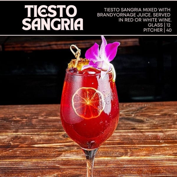 A glass of Tiesto Sangria, garnished with a purple orchid and dried orange slice, on a wooden table.