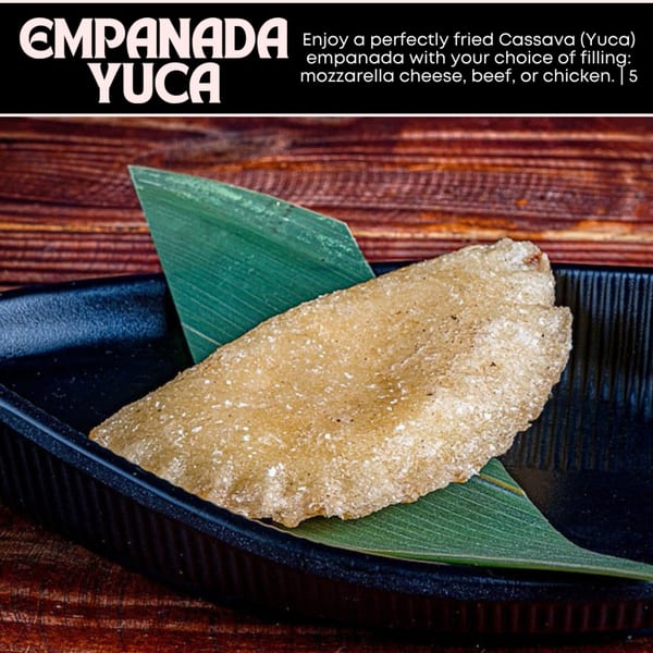 Golden-fried cassava empanada on a dark plate with a green leaf garnish, against a wooden background.