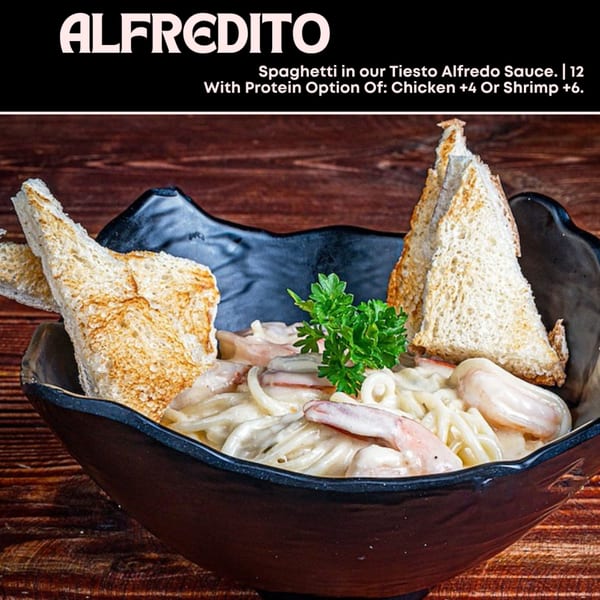 Alfredito spaghetti with shrimp, creamy sauce, parsley, and toasted bread in a black bowl.