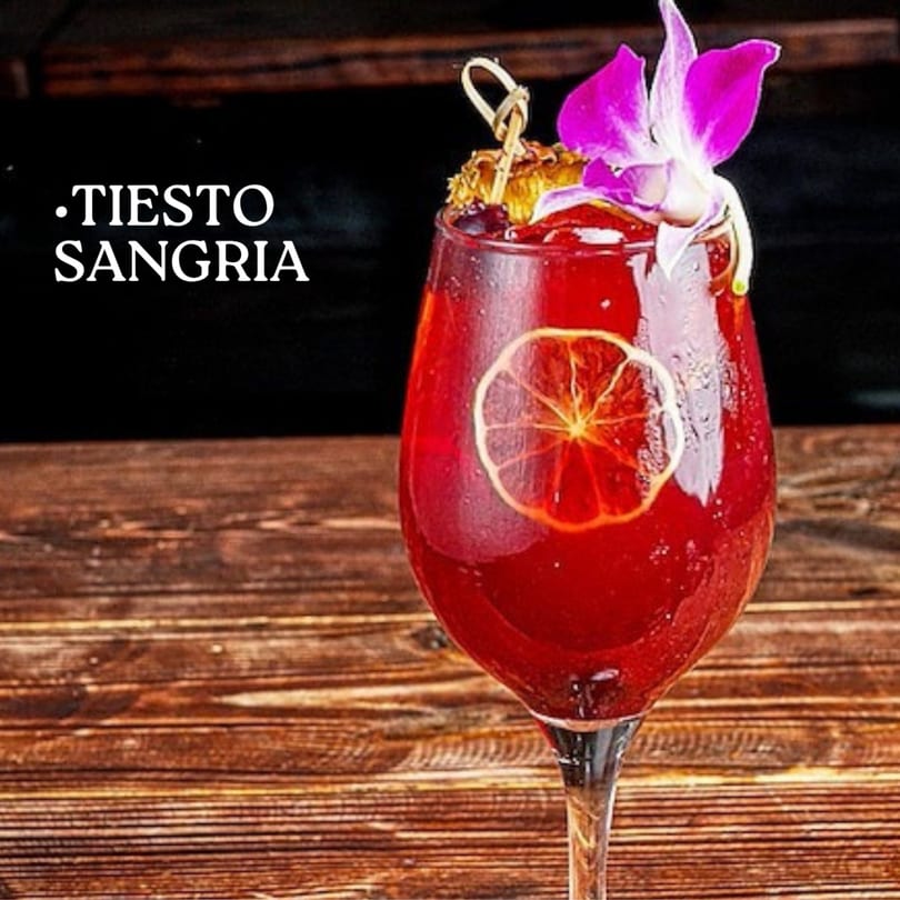 A glass of red sangria, garnished with a purple orchid and dried orange slice, on a wooden table.