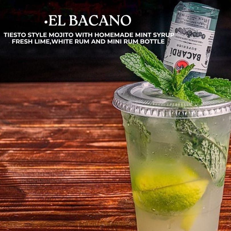 A mojito with mint, lime, and a mini Bacardi rum bottle, on a wooden surface.