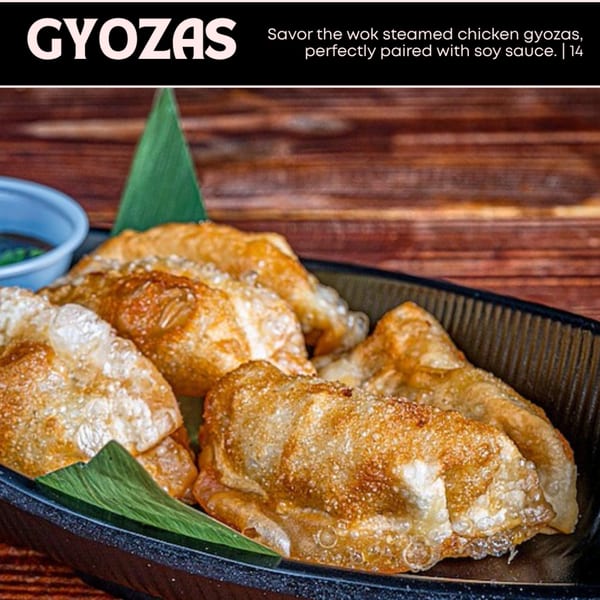 Golden-brown chicken gyozas with a side of soy sauce, garnished with a green leaf.