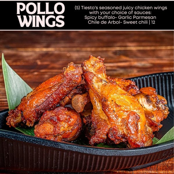 Five crispy, golden-brown chicken wings with green garnishes in a black bowl on a wooden table.