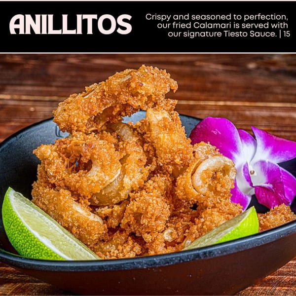 Crispy fried calamari rings with lime wedges and a purple orchid in a black bowl.