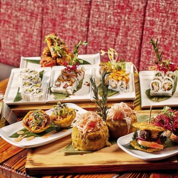 A vibrant spread of Latin-American dishes, including sushi rolls, plantain cups, and mofongo, on a wooden board.