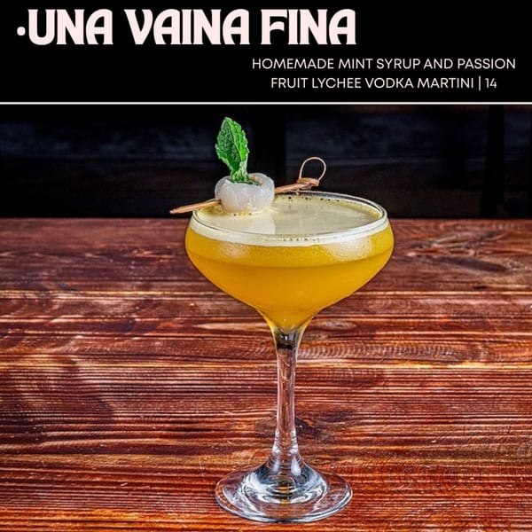 A yellow martini with foam, garnished with a lychee and mint leaf, on a wooden table.