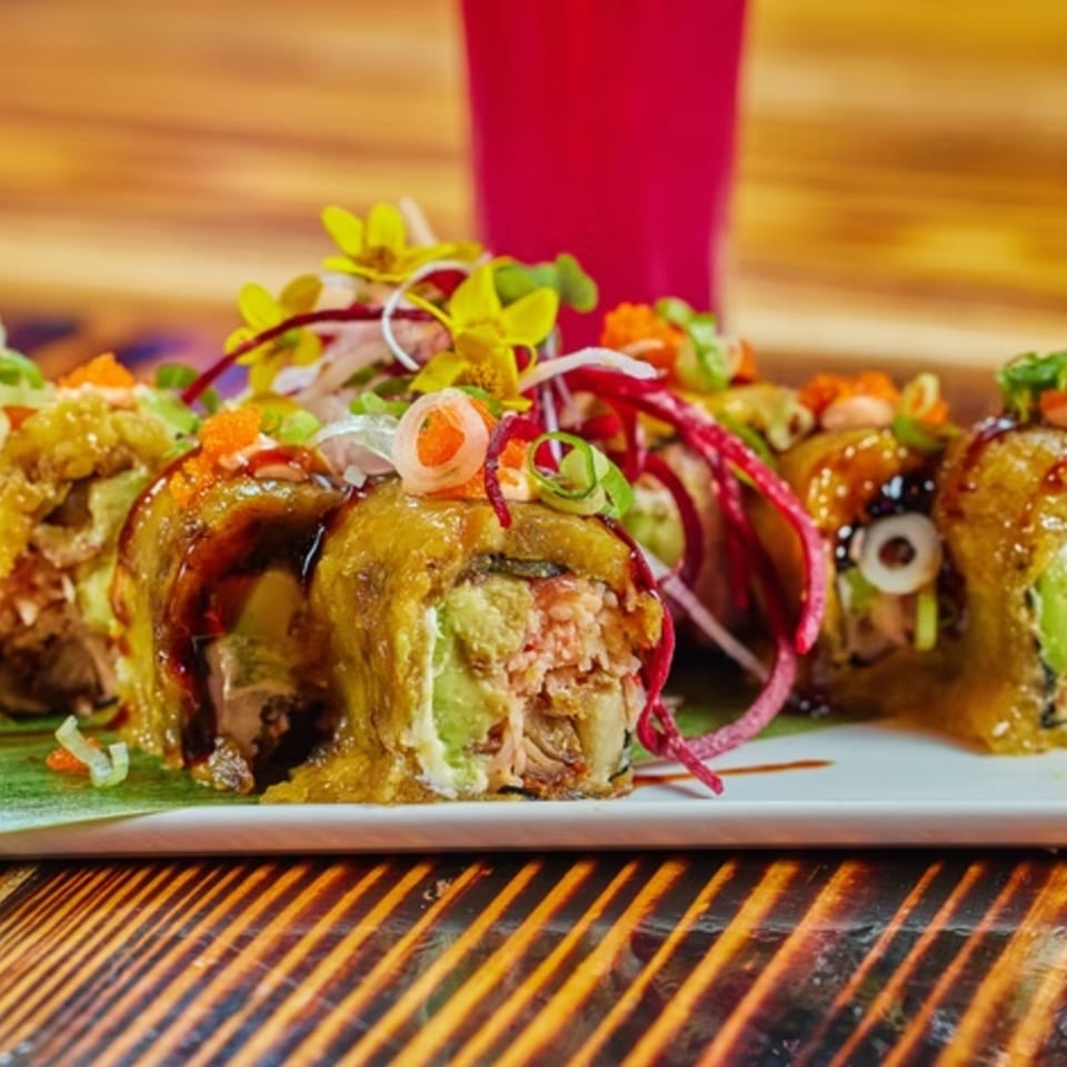 Latin-American sushi rolls with avocado, sauce, and colorful garnishes on a white plate.