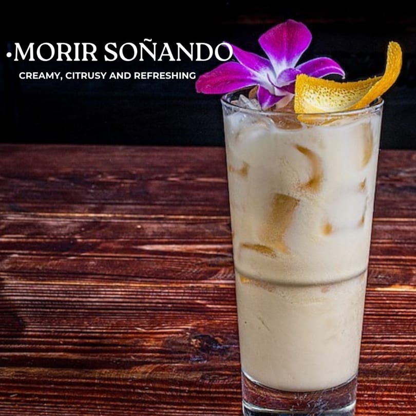 A creamy, citrusy Morir Soñando drink with ice, garnished with an orchid and orange peel.