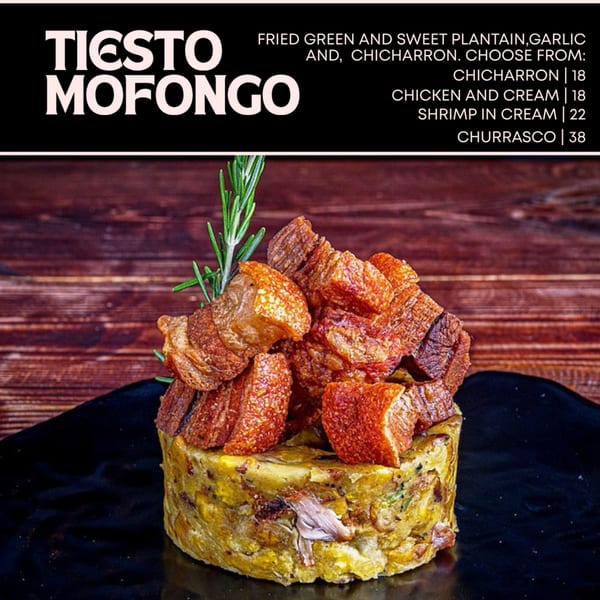 Tiesto Mofongo with crispy chicharron and a rosemary sprig on a dark plate.
