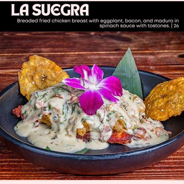 Breaded fried chicken breast with eggplant, bacon, maduro, spinach sauce, and tostones, garnished with a purple orchid.